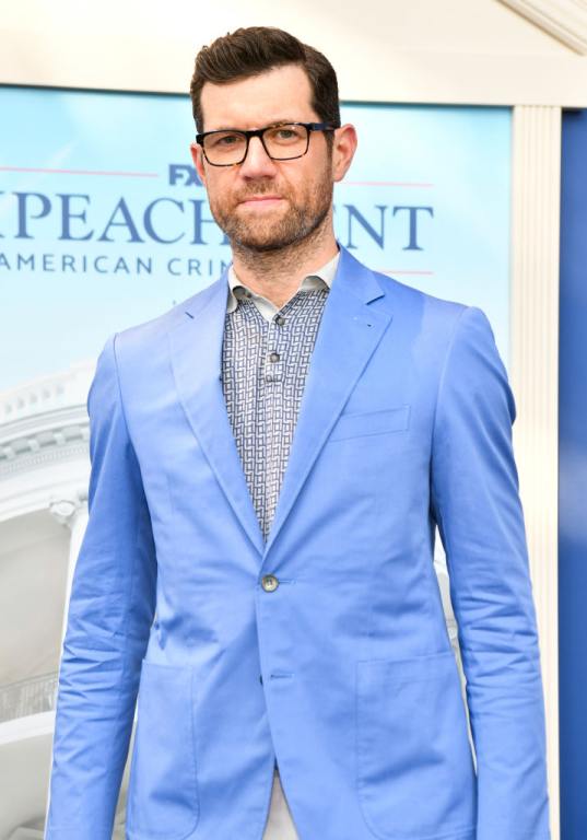 Billy Eichner wearing a bright blue blazer over a graphic collared undershirt wearing black framed glasses.