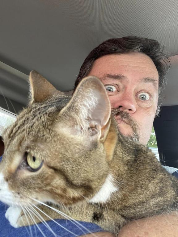 Jim O'Brien and his cat in a car. The cat is hogging the camera. Used in an article on Gen Alpha and mewing.