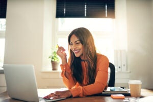 Female entrepreneur working on a laptop while sitting at a table in her home office. This story is about work-at-home opportunities.