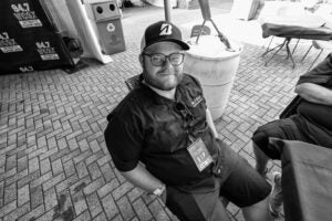 Black and white photo of Ryan Logan sitting in a chair wearing WCSX gear backstage of Pine Knob