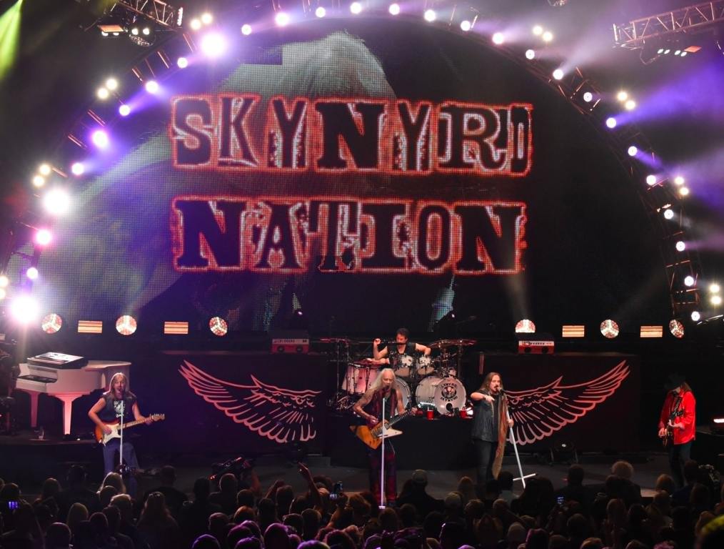 Lynyrd Skynyrd concert backdrop reading "Skynyrd NAtion" with band members performing on stage at Pine Knob.