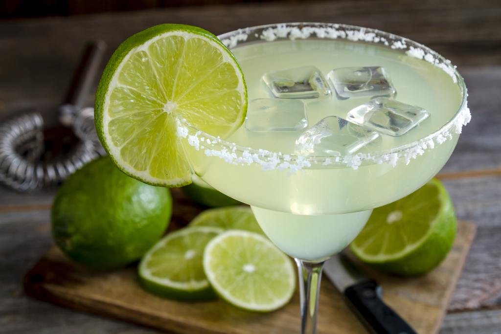 Classic lime margarita cocktail with sliced and whole limes sitting on wooden cutting board