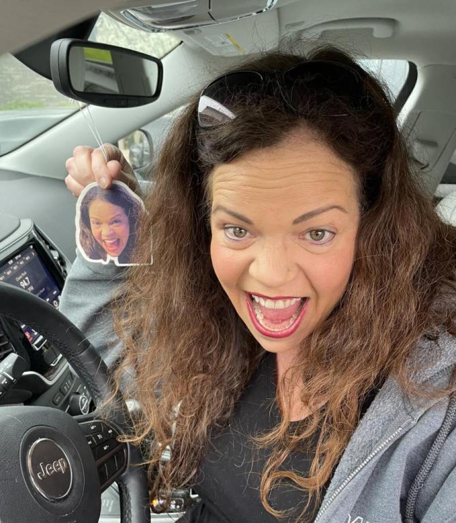 a woman sitting in her car smiling next to an air freshener that is also a picture of her face. Used in an article (among others) on Facebook groups