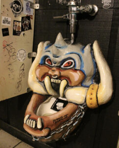 a urinal with an art installation of Motorhead's Snaggle Tooth