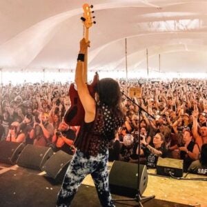 guy holding up his bass guitar while looking out at a packed crowd