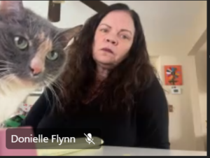 A woman is participating in a group online meeting from home when her cat sticks its head in the video frame.