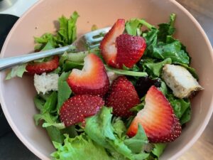 a bowl of salad with greens, grilled chicken, and sliced strawberries.