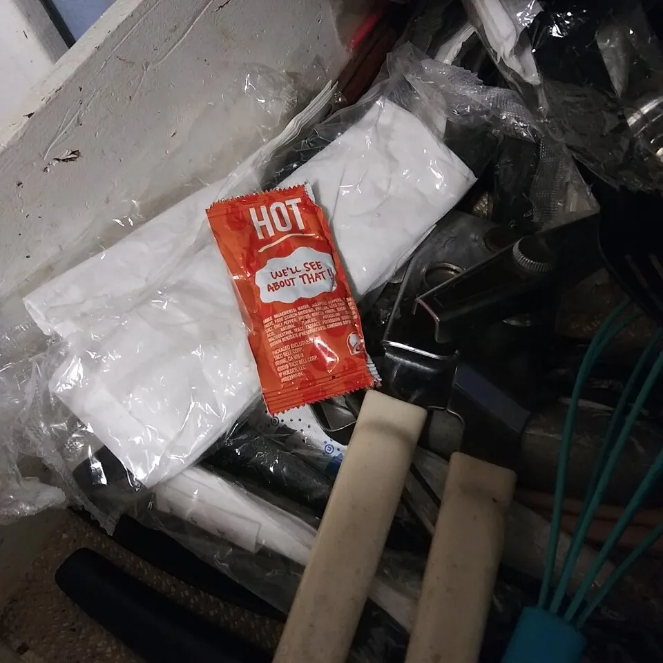Photo of a Taco Bell sauce packet in a kitchen drawer. with other utensils 