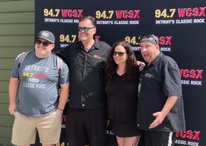 four people standing in front of a WCSX banner outside. The crew is tailgating at Pine Knob.